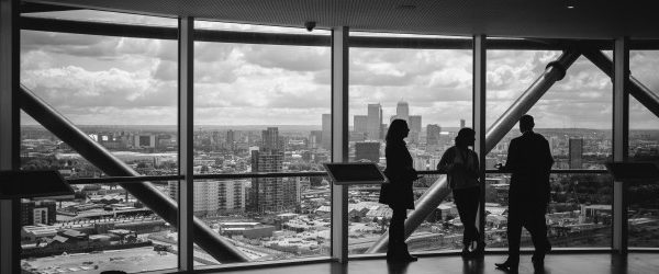 Group of three standing at window looking out onto a city landscape